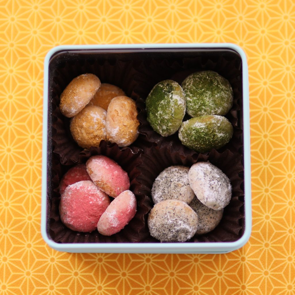 抹茶、きな粉、いちご、黒ごまの4種スノーボールクッキーが詰まった正方形の缶。黄色の和柄背景。