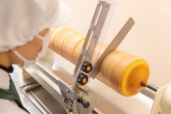 職人が焼き上げたバウムクーヘンを専用カッターで均等に切り分けている様子