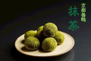 抹茶味のネガイノヒトツブ。枡に盛られた米の上に、金色のフォークで一粒をのせた和ポルボロン。
